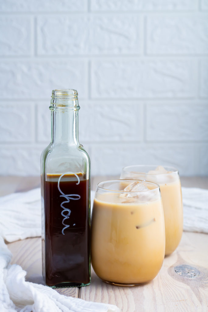 Two glasses of iced chai next to a bottle of chai concentrate.
